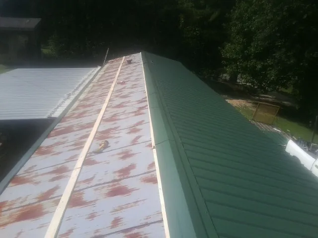 Old rusted panels beside newly installed green metal roofing — Wind Damage Roof Repair by Roofing Brothers in Williamsburg