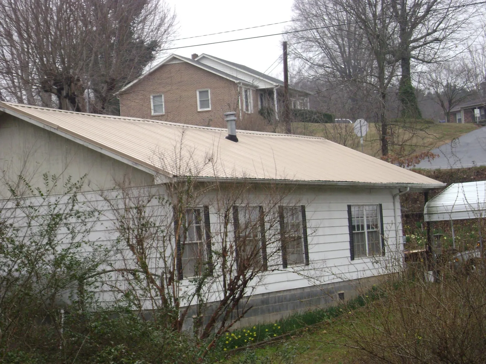 Tan metal roof on a white sided house set into a hillside — Commercial Roofing by Roofing Brothers in Williamsburg